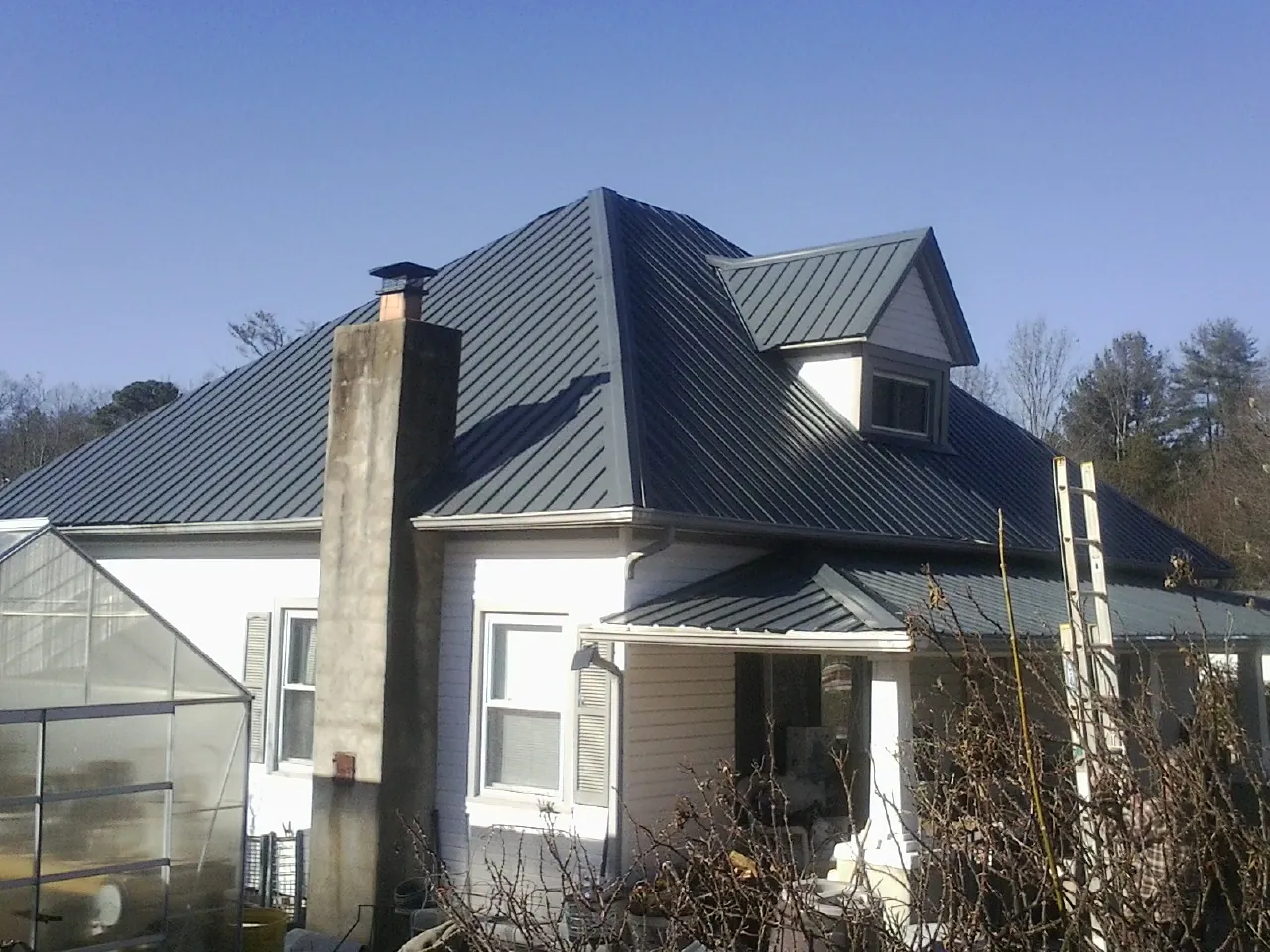 Dark blue standing seam metal roof on a white farmhouse with dormer — Slate & Tile Roof Repair by Roofing Brothers in Crewe