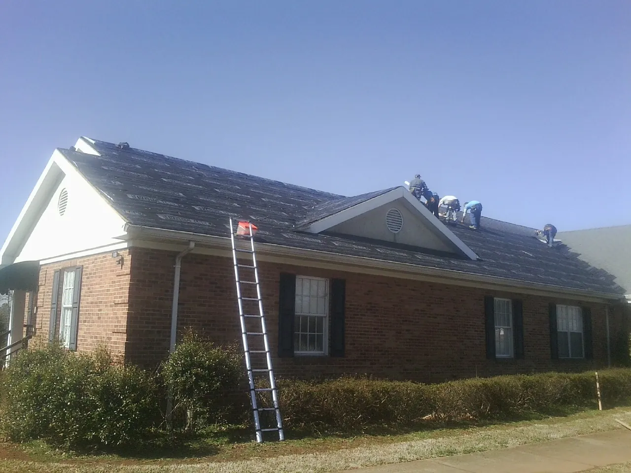 Crew tearing shingles off a brick ranch roof with a ladder set — Emergency Roof Repair work by our crew in Crewe