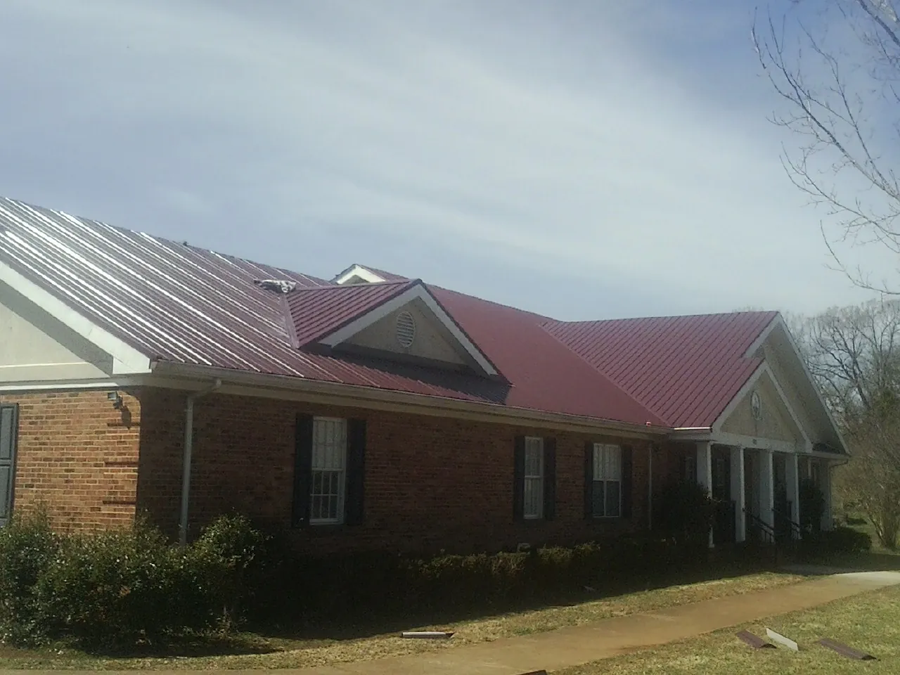 Red metal roof with gabled entries on a long brick building, from a Hail Damage Roof Repair job in Crewe