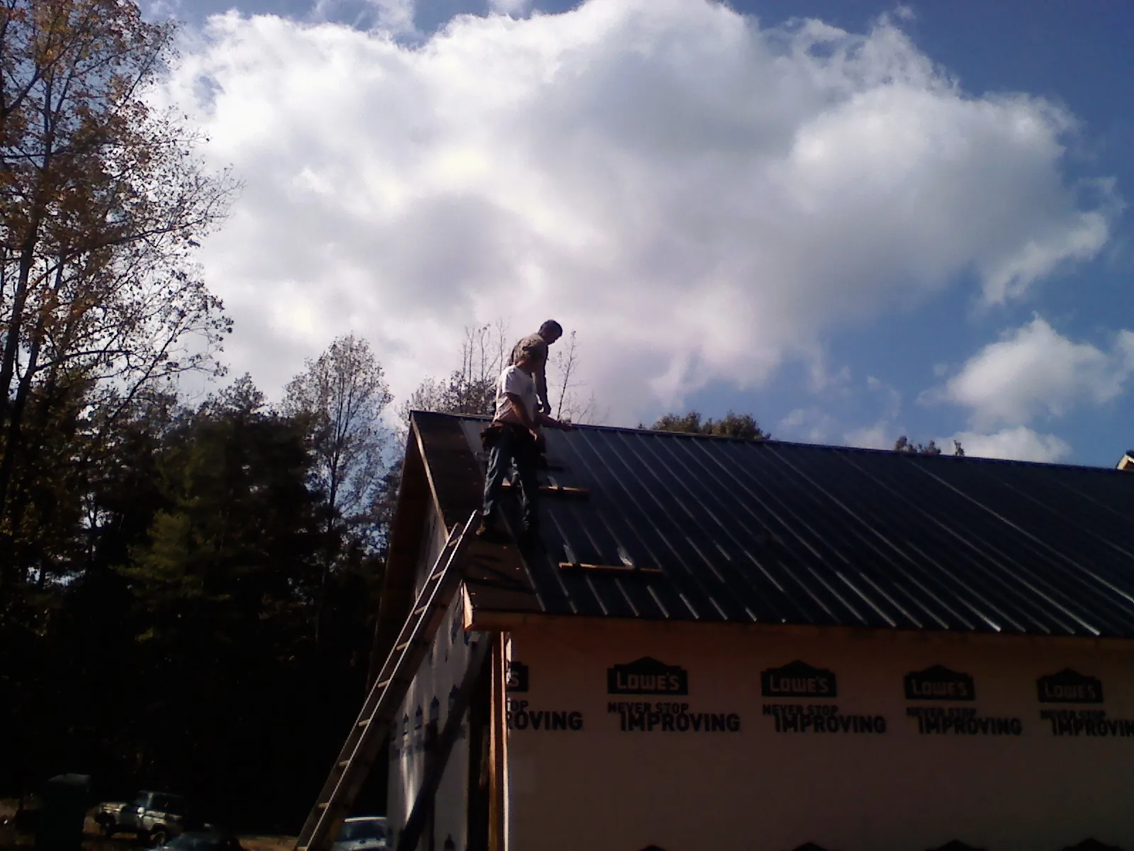 Roofer fastening dark metal panels high against a cloudy sky, from a Roof Inspection job in Crewe