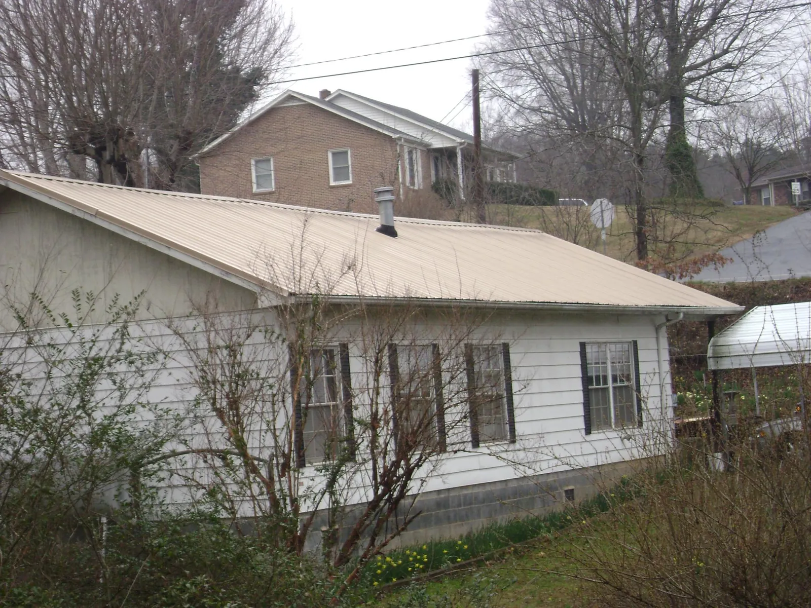 Tan metal roof on a white sided house set into a hillside — Commercial Roofing by Roofing Brothers in Crewe