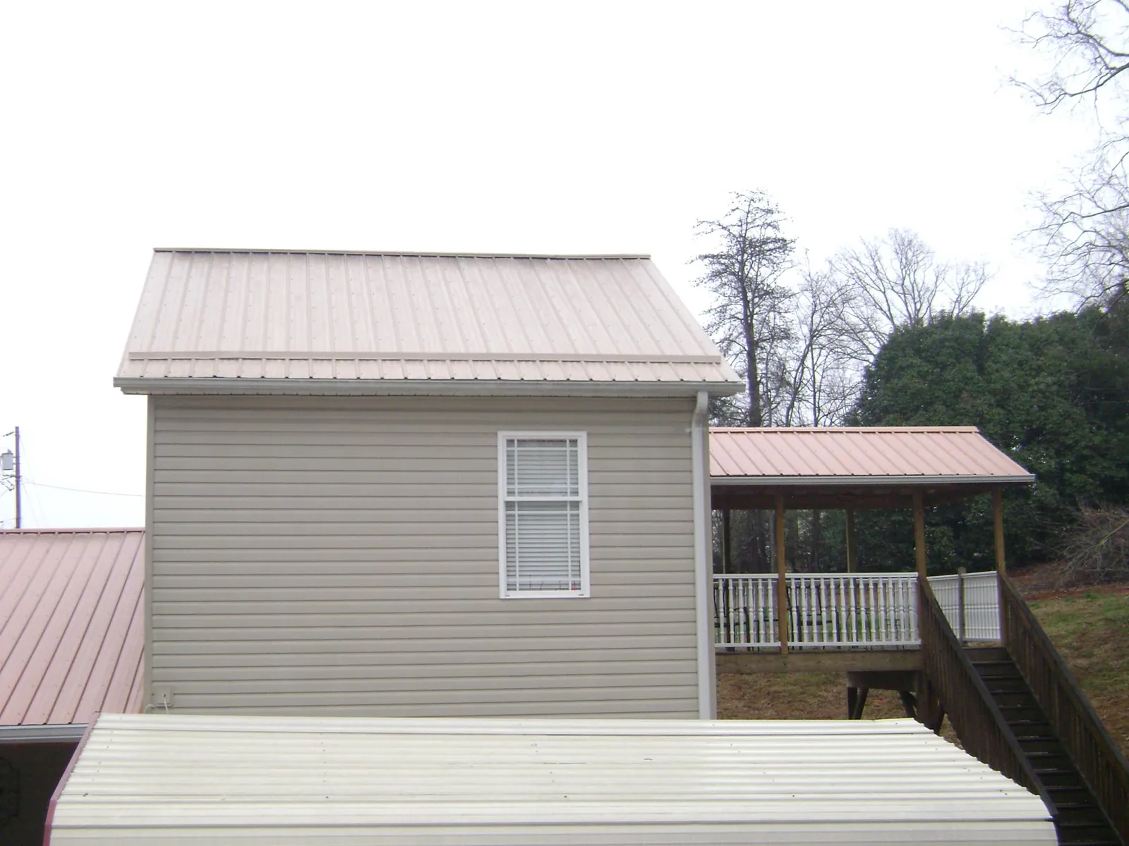 Tan metal roofs on a two story addition and attached porch, from a Roof Replacement job in Crewe