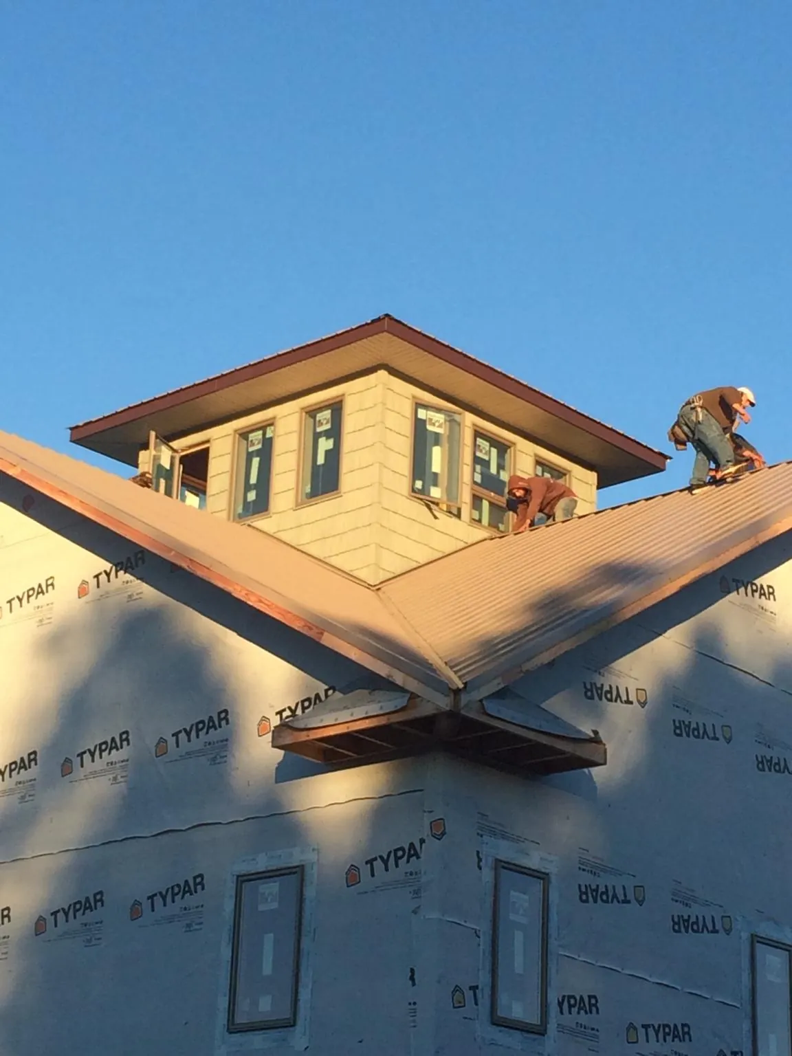 Roofers working around a rooftop cupola on a new metal roof at sunset — Roof Waterproofing in Crewe by Roofing Brothers